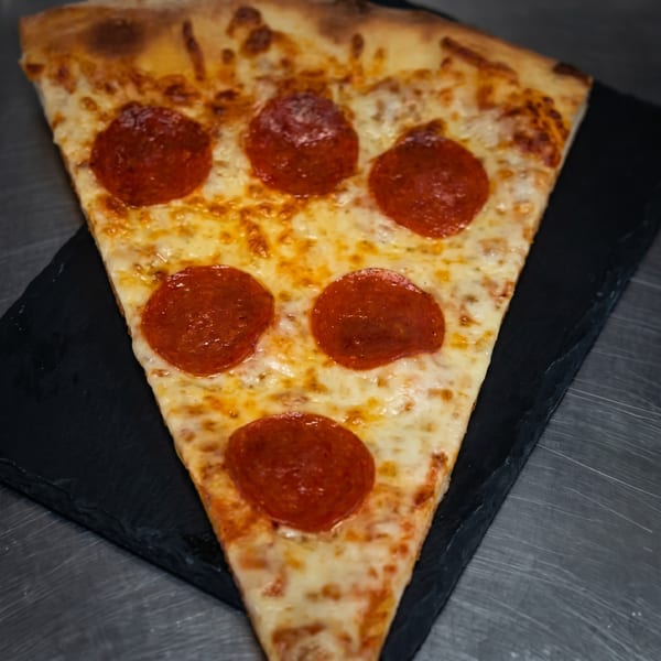 A large slice of pepperoni pizza with melted cheese on a dark serving board.