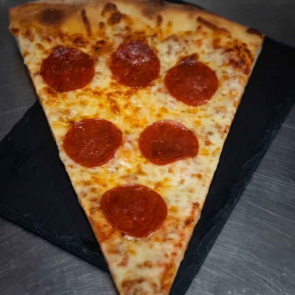 A large slice of pepperoni pizza with melted cheese on a dark serving board.