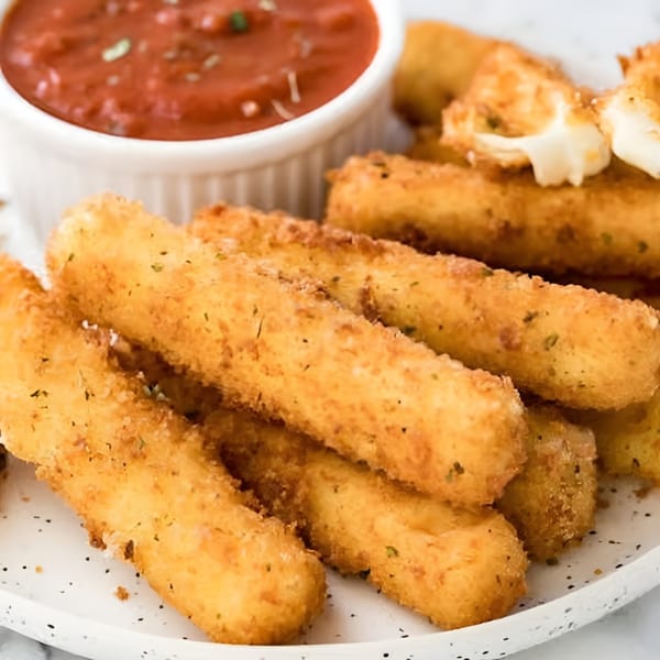 Golden-brown mozzarella sticks, one broken open with melted cheese, served with a side of marinara sauce.