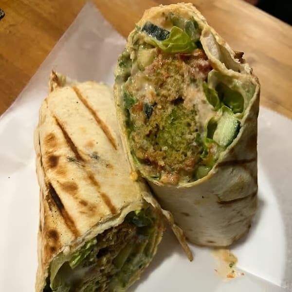 Two halves of a falafel wrap, filled with green falafel, lettuce, and sauce, on a white plate.