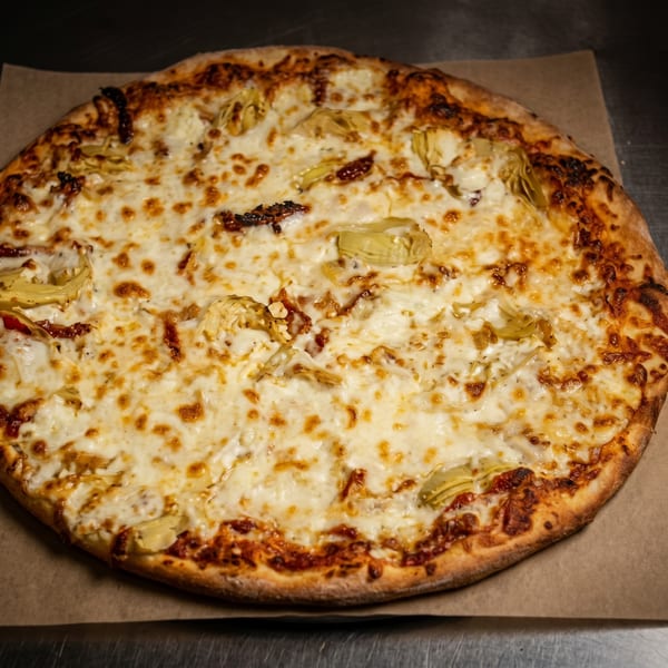 A whole round pizza with melted cheese, artichoke hearts, and sun-dried tomatoes on a brown paper.