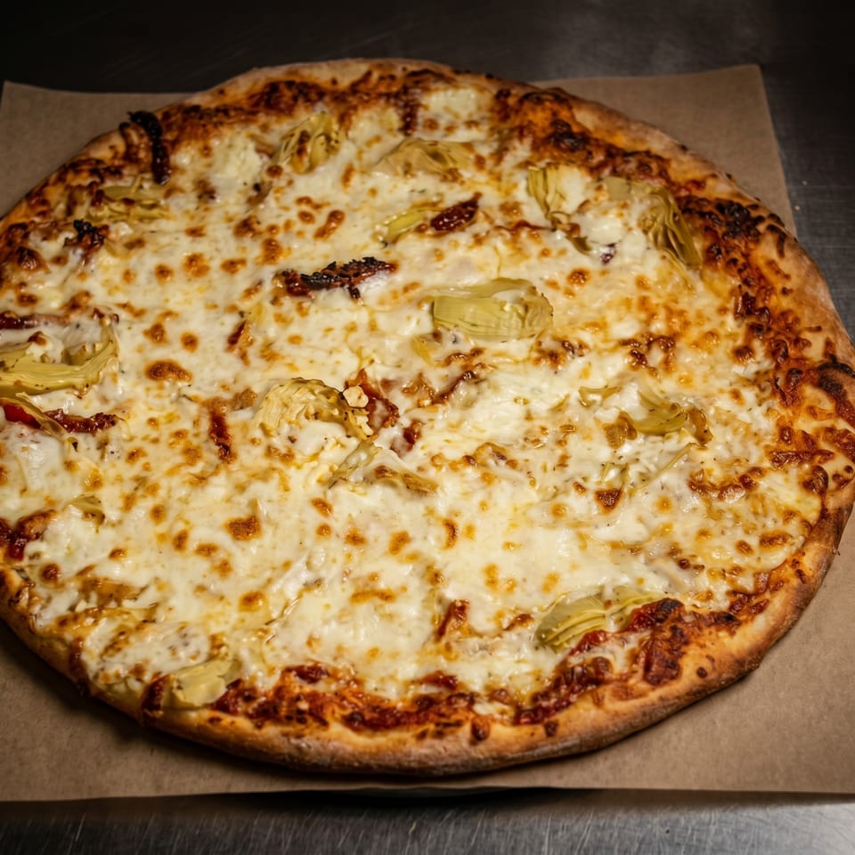 A whole round pizza with melted cheese, artichoke hearts, and sun-dried tomatoes on a brown paper.